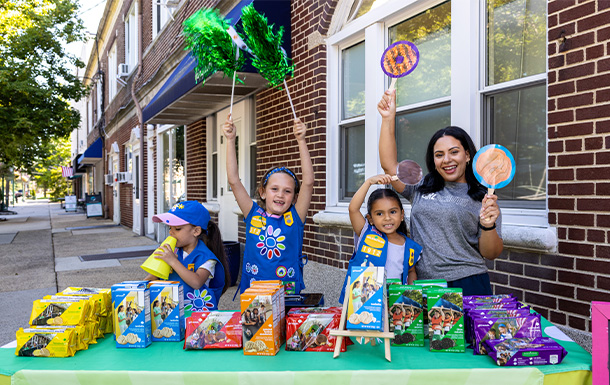 Girl Scouts and a troop leader holding up cookie signs and pompoms at a cookie booth