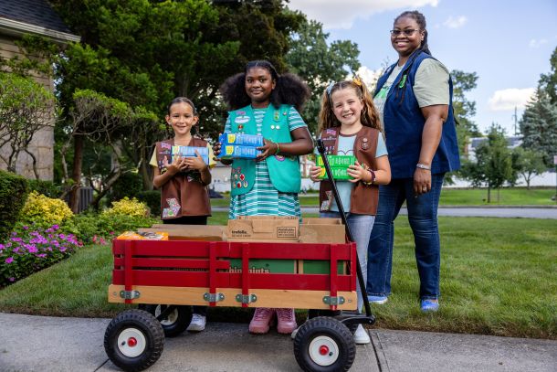 Girl Scouts and a troop leader behind a wagon full of cookies